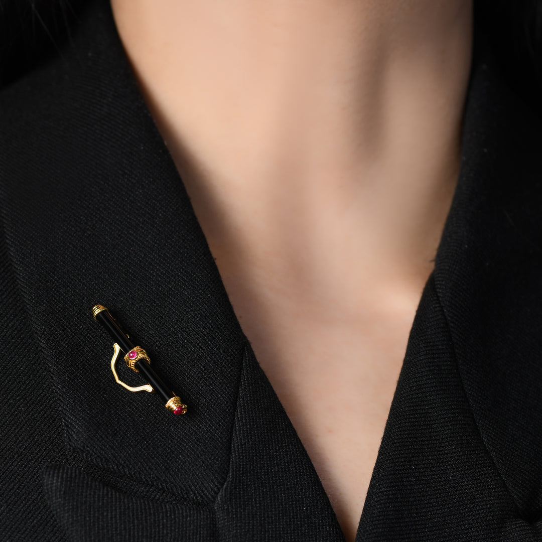 Introducing our exquisite brooch, where elegance meets sophistication. Crafted with a central stick-shaped black agate, adorned with rubies delicately nestled on a spiral-shaped golden design at both ends and middle. A geometric line bridges gracefully across the top, elevating the piece to a new level of refined charm.