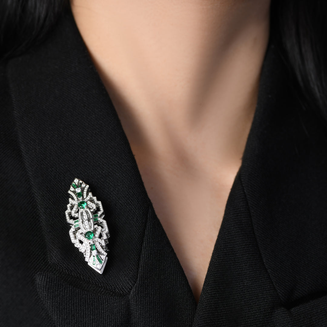 Introducing our versatile Art Deco-inspired brooch adorned with clear geometric lines, fully encrusted in shimmering white melee diamonds and accented by stunning emeralds. This unique piece not only exudes elegance with its intricate design but can also transform into two individual lapel pins, offering versatility for a variety of styling options.