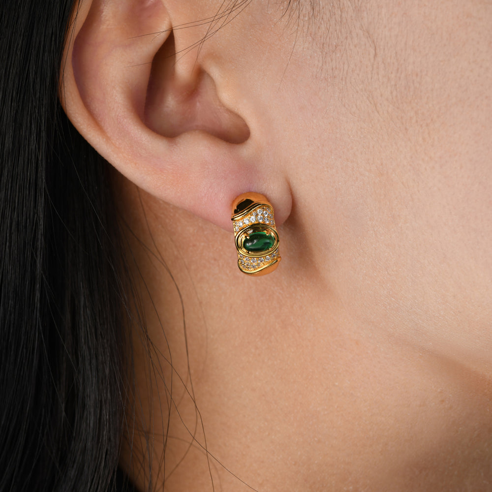 Elevate your style with our sculptural chunky hoops adorned with a captivating oval emerald. The metal surface is enhanced by two elegant arcs, creating a striking contrast in texture, while clustered simulated diamonds add a touch of timeless sparkle to these exquisite earrings.