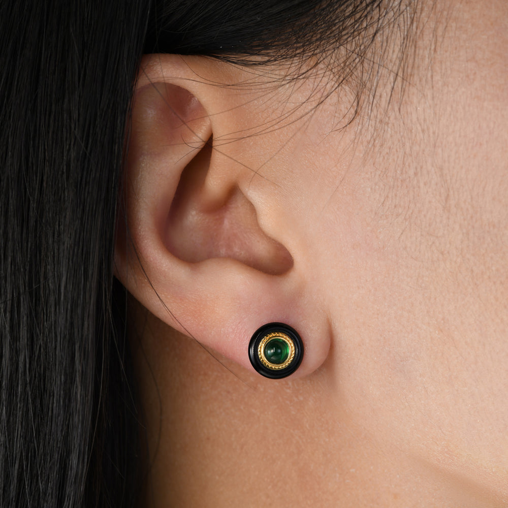 Crafted with precision, the outer ring features sleek black agate, the middle ring boasts a textured golden surface, and the innermost circle dazzles with a round emerald, creating a sophisticated and eye-catching accessory.