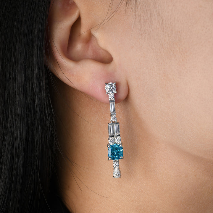 Immerse yourself in the allure of our earrings showcasing a captivating cushion-cut blue simulated diamond as the centerpiece. Enhanced by complementary white diamonds in varying shapes, this pair elegantly captures a harmonious blend of sophistication and brilliance, making it a standout addition to any ensemble.