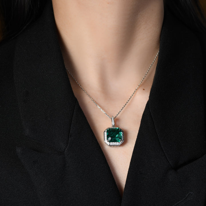 Experience timeless beauty with our exquisite pendant, where a resplendent emerald takes center stage, encircled by delicate round simulated diamonds. The Asscher-cut-shape metal base adds a touch of sophistication, while a dainty ring, inlaid with diamonds, graces the top, creating a perfect blend of luxury and elegance in one captivating piece.