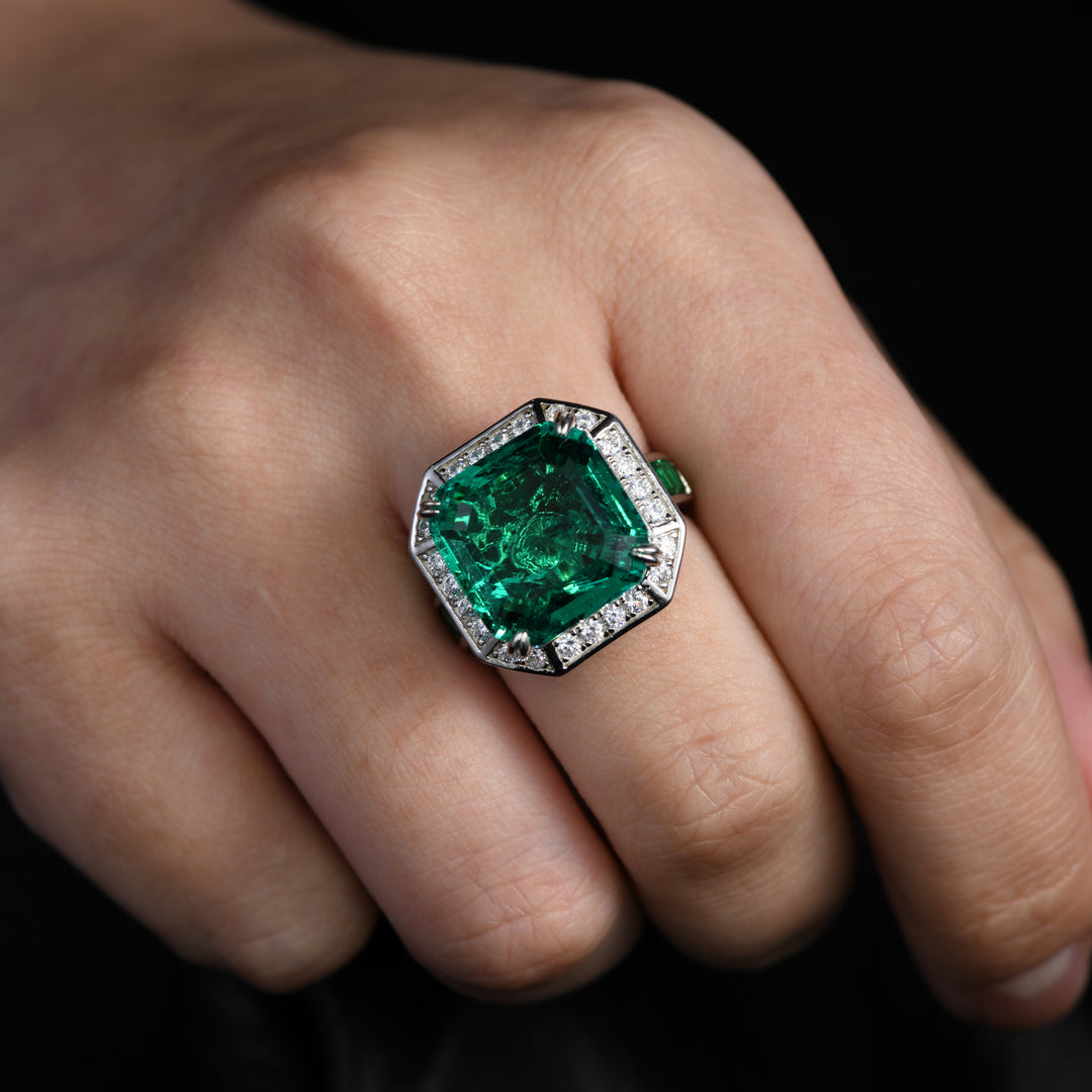 This ring features a sizable Asscher-cut emerald as the centerpiece, delicately nestled on a unique stage. The stage, adorned with white diamonds, and the band, inlaid with small emeralds, create an elegant and classic design, making this ring a sophisticated accessory that seamlessly blends vintage charm with modern style.